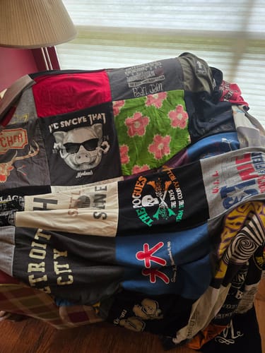 Close-up of a customer's Premium T Shirt Quilt draped over a chair, showing a variety of colorful graphic patches.