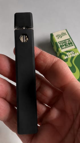 A reviewer holds the black ROLLZ THCA Vape in their hand, with the green product box visible in the background.