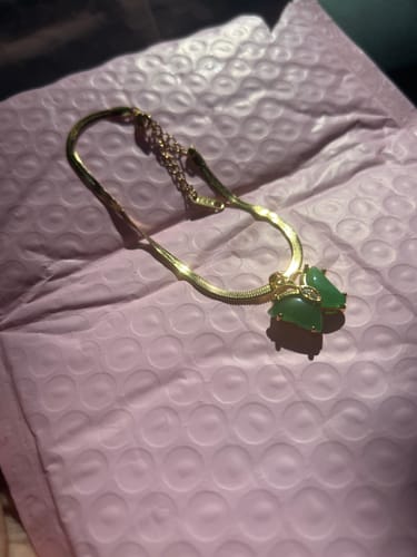 Customer's Jade Butterfly Anklet with a gold chain and green butterfly charm, lying on a pink mailer.