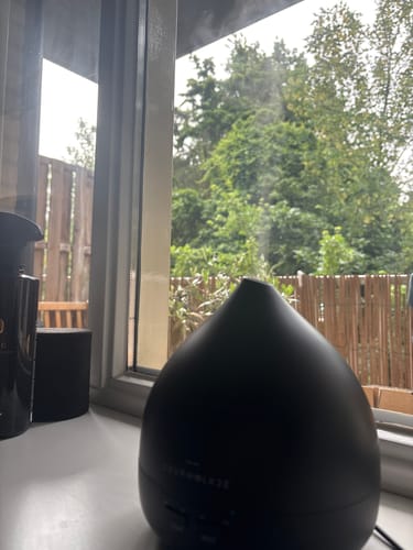 Recensent toont de matzwarte Unity 2.0 Aroma Diffuser die nevel verspreidt op een vensterbank.