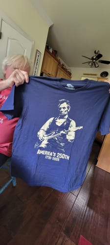 Customer holds up a blue Lincoln 250 T-Shirt showing a graphic of Abraham Lincoln playing an electric guitar.