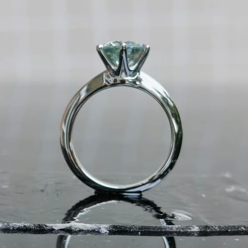 Customer's Doveggs classic 6-prong solitaire ring with a light blue stone, shown from the side on a reflective surface.
