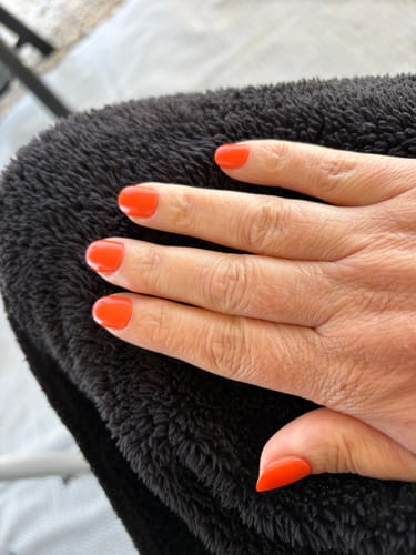 Nahaufnahme der Hand einer Kundin mit leuchtend orangen 'Tempting Tangerine' UV-Gel-Nagelfolien.