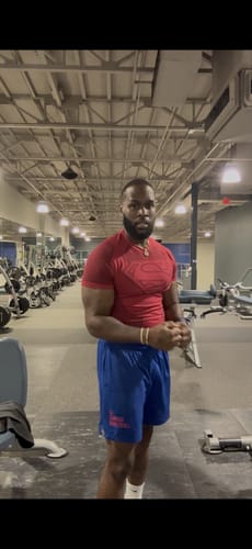 Reviewer in a gym wearing the red Superman Compression Tee, showing its tight, athletic fit.