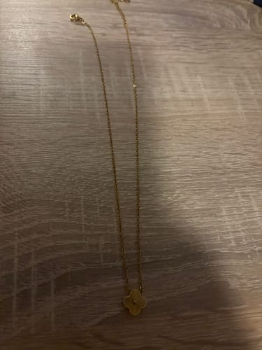Die goldfarbene Plain Clover Kette eines Kunden, die auf einer Holzoberfläche liegt.