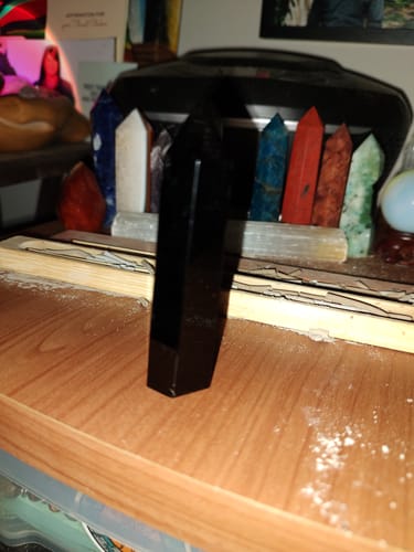 Customer's black Obsidian Mini Point from the promo set standing on a wooden desk with other crystals in the background.