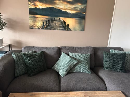 Anmelderens flaskegrønne flettede velurputetrekk i en grå sofa.