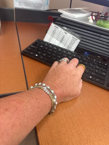 Customer wearing a stack of waterproof bracelets with gold and pearl details at a desk.