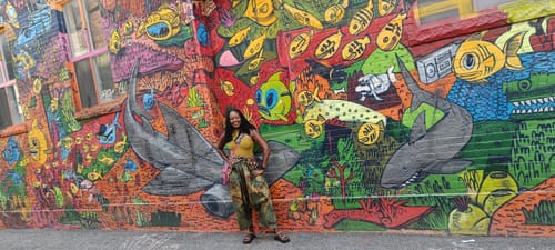 Reviewer posing outdoors in the retro tie-dye cotton harem pants in front of a colorful mural.