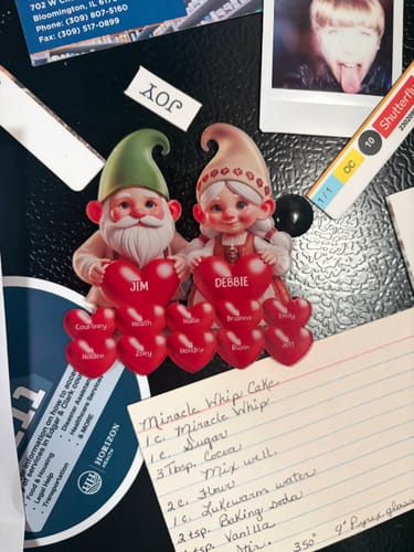 Customer's personalized gnome magnet on a fridge, showing grandpa and grandma gnomes with hearts for grandchildren's names.