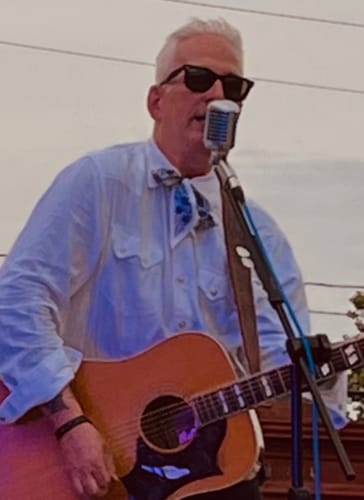 Customer wearing the Motif Skinny Scarf tied as a bow while performing with a guitar.