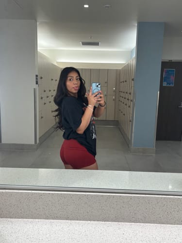 Reviewer taking a mirror selfie to show the fit of the red Olympia Shorts in a locker room.
