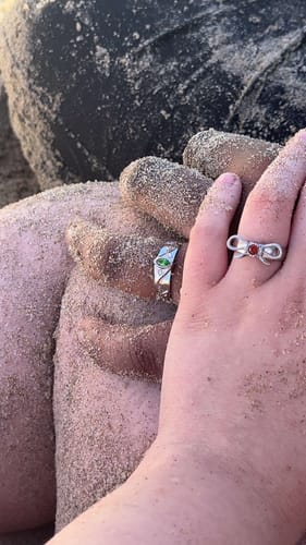 Customer's close-up of two sandy hands, each wearing a different silver Birthstone Ring on a beach.