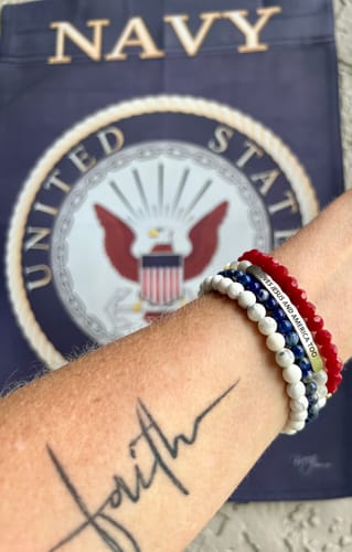 Reviewer's wrist showing a stack of red, white, and blue accent bracelets in front of a Navy flag.