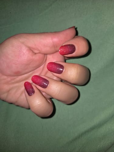 Hand einer Kundin, die die glitzernden 'Taunted' UV-Gel-Nagelfolien mit einem rot-bordeauxroten Farbverlauf trägt.