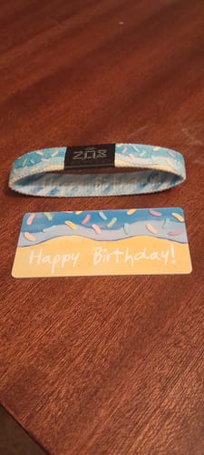 Customer's light blue Happy Birthday Bracelet with a sprinkle pattern, shown next to its matching collector's card on a wooden surface.