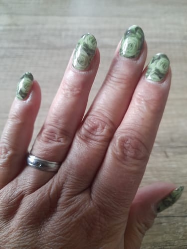 Die Hand einer Kundin mit den UV-Gel-Nagelfolien 'Sage Rose' in einem glänzenden salbeigrünen Design.