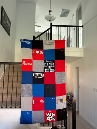 Customer's Project Repat T-Shirt Quilt made from Chick-fil-A shirts, hanging over a staircase railing in a home.