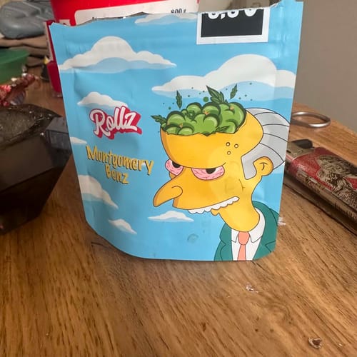 Customer's pouch of Montgomery Benz THCA Flower with cartoon packaging on a wooden table.