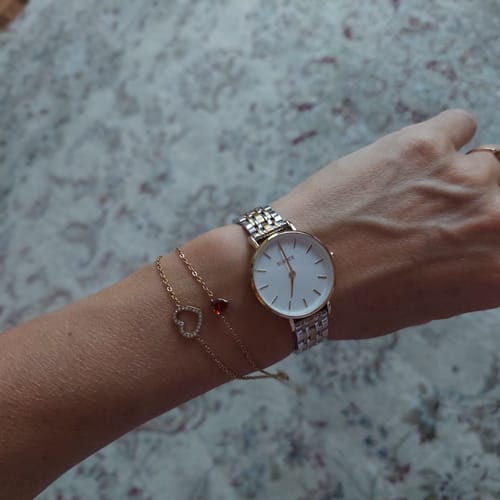 Customer's wrist wearing the Ruby Petite Gold Silver watch with two delicate gold bracelets against a floral background.