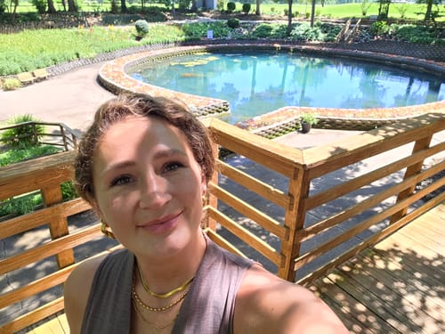 Reviewer in a sunny outdoor setting wearing layered gold necklaces and earrings from the WaterProof Jewelry Bundle.
