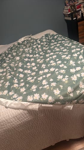 Customer's Sage Wildflower Blanket with a floral print spread out on a white textured bedspread.