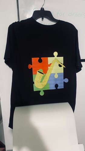 Reviewer's finished black t-shirt with a vibrant saxophone and puzzle design, created with the DTF powder.