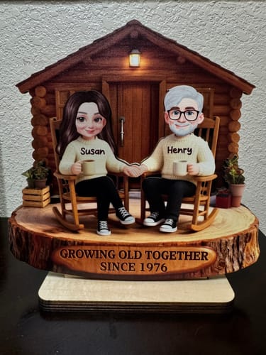 Customer's personalized wooden plaque of a couple in front of a cabin, engraved with 'Growing Old Together Since 1976' on the base.