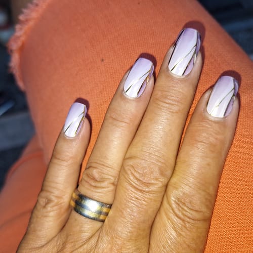 Kundin zeigt ihre „Pearl Puzzle“ UV-Gel-Folien. Die lila-weiße Maniküre mit Goldlinien hält seit zwei Wochen.