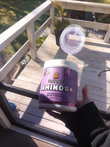 Reviewer holding a purple tub of UGLYFACE® AMINOS+ in their hand outdoors.