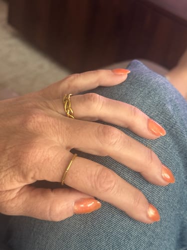 Reviewer's hand wearing the two gold Naxos rings from the bundle on separate fingers against a denim background.