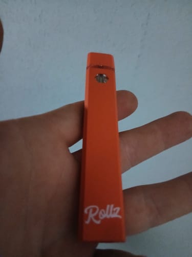 Customer holding the bright orange ROLLZ THCA Vape in their hand against a plain wall.