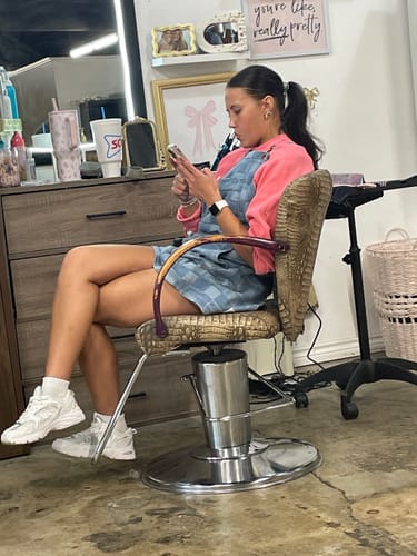 Reviewer in a salon chair wearing the light-blue denim The Whitmore apron.