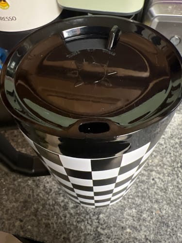A customer's black ONE Lid shown on top of a checkered Thicc Buddy 40oz tumbler, with the drinking spout closed.