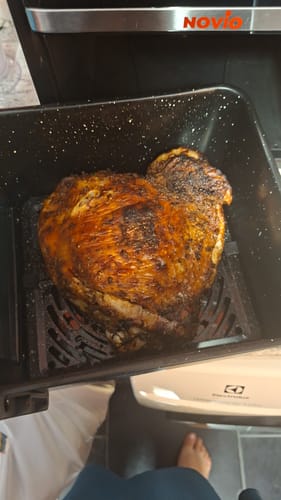 Reviewer showing a whole, golden-brown chicken cooked in the basket of the Air Fryer Novio StonePro.
