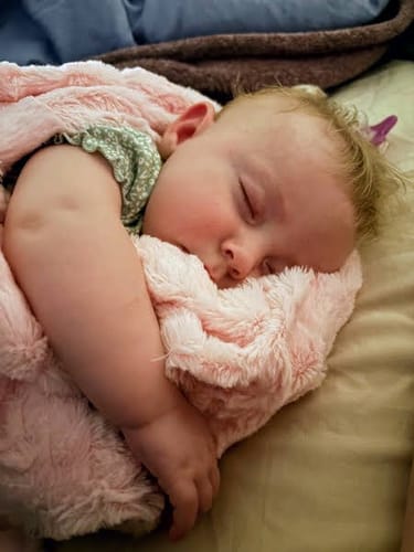Customer shows a baby sleeping soundly, cuddled with the soft Sorbet True Pink Blanket.