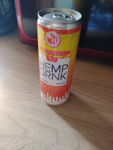 Reviewer's can of the Peach Hibiscus hemp drink sitting on a wooden table.