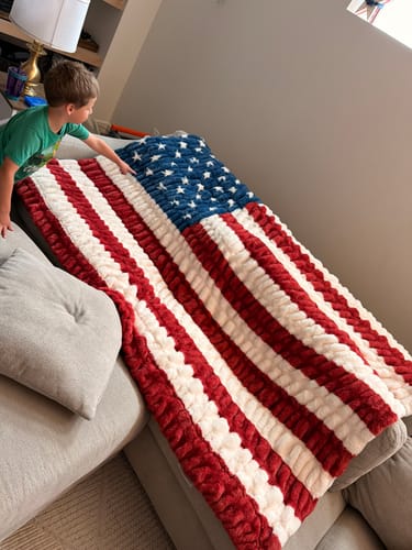 Customer's child touching the plush, patriotic Hugs Flag Blanket draped over a couch.