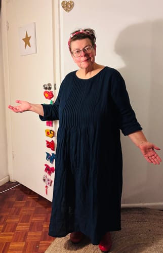 Reviewer showing the fit of the long-sleeved, dark blue shirred cotton dress indoors.