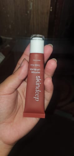 Customer holding a dusty rose tube of Skindeep Peptide Lip Glaze.