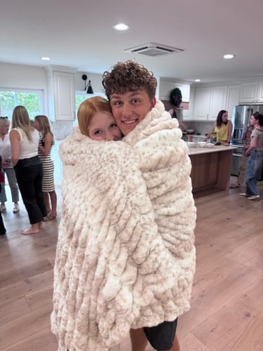 Customer photo of two people smiling while wrapped together in the plush Hugs Cream Fawn Blanket.