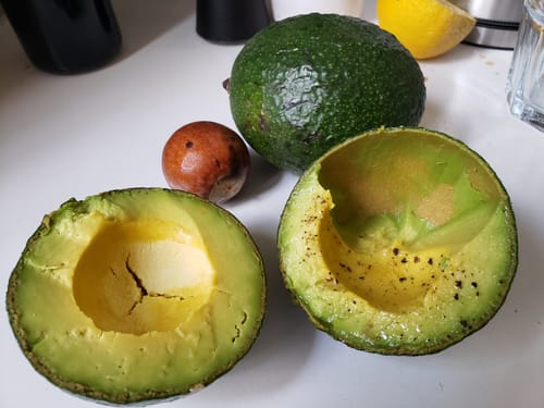 Rezensent zeigt eine aufgeschnittene Reed Bio Avocado mit cremigem Fruchtfleisch und entferntem Kern.