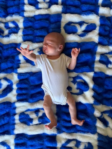 A newborn baby sleeping on the reviewer's soft, blue and white checkered BYU Cougars Blanket.