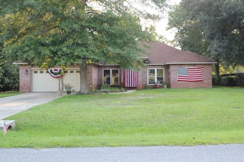 Customer's brick house with the Heavy Duty American Flag hanging vertically near the entrance and another flag on the right wall.
