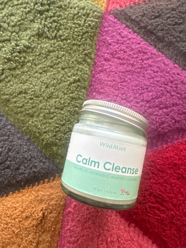 A customer's jar of WildMint Calm Cleanse displayed on several colorful, textured towels.