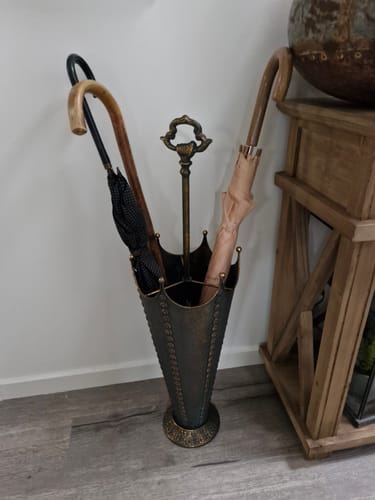 Customer's Louna French Provincial Umbrella Stand in antique gold, holding three umbrellas against a wall.