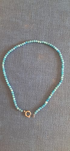 Un client montre son collier Apatite Bleue aux perles harmonieuses posé sur une surface bleue unie.