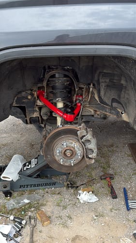Customer installing the bright red upper control arm from the Suspension Lift Kit on their truck's front wheel.