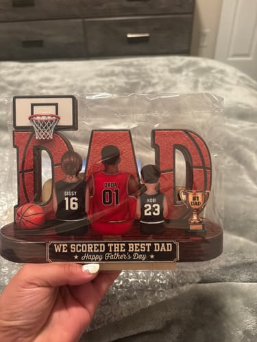 Customer holding their personalized basketball 'DAD' plaque, showing figures of a father and two kids on its wooden base.