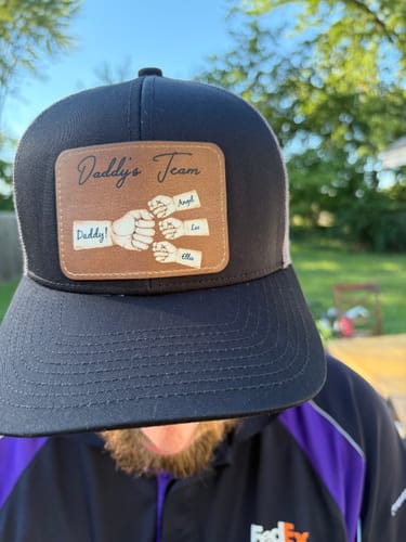 Reviewer wearing the black Daddy's Team hat with a personalized leather patch showing a fist bump for Daddy, Angel, Lee, and Ella.
